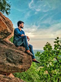 Man sitting on rock against sky