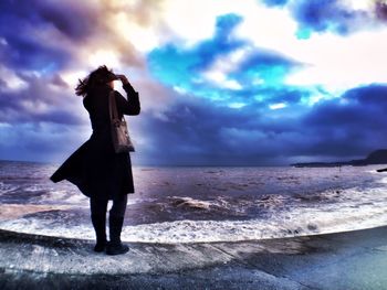 People standing on beach against cloudy sky