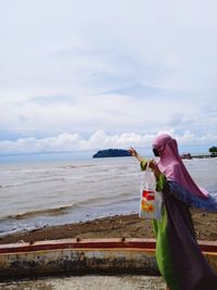 Rear view of woman standing at beach against sky