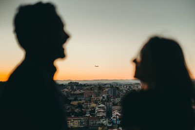 Silhouette couple standing against city during sunset