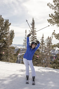 Portrait of woman with arms raised skiing on snow covered land