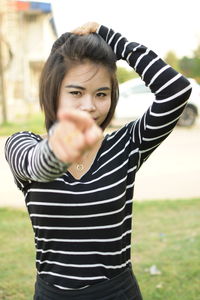 Portrait of smiling young woman with hand in hair gesturing while standing at park
