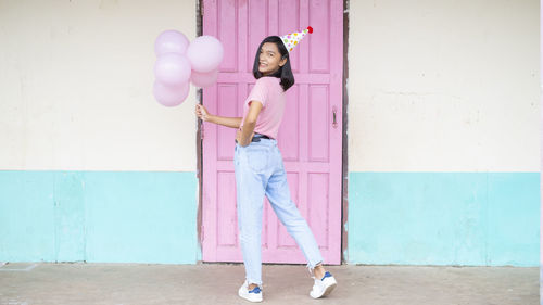 Full length of woman with pink umbrella standing against wall