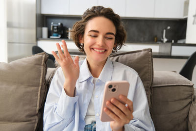 Young woman using mobile phone while sitting on sofa at home