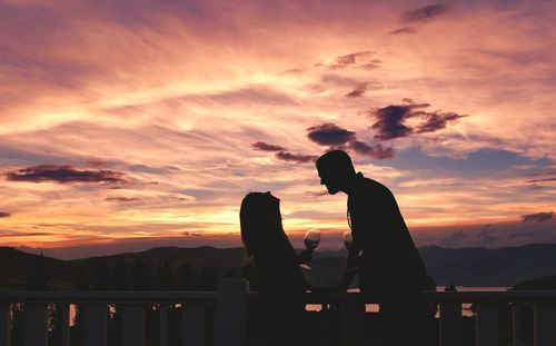 Silhouette men sitting on railing against sky during sunset