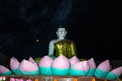 Statue of illuminated buddha against sky at night