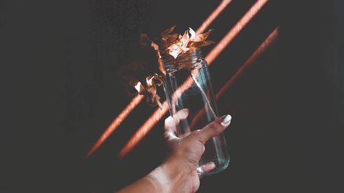 Midsection of person holding illuminated lighting equipment against black background