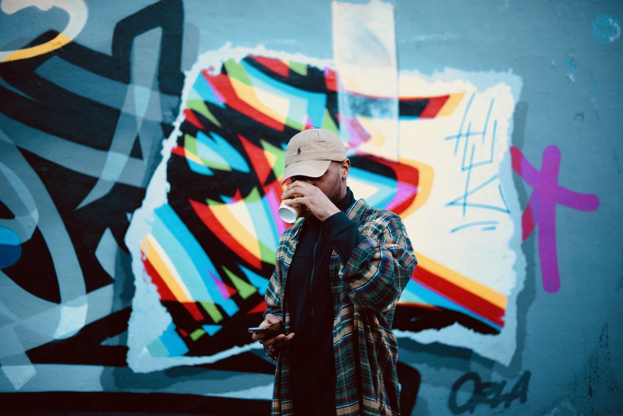 MIDSECTION OF PERSON HOLDING UMBRELLA STANDING AGAINST MULTI COLORED BACKGROUND