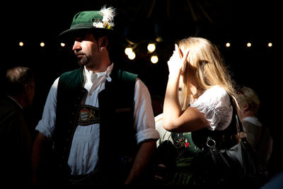 Man and woman wearing hat while standing against black background