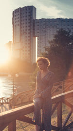 Woman sitting on railing in city during sunset