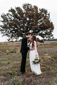 Newlywed couple kissing while standing on grassy land