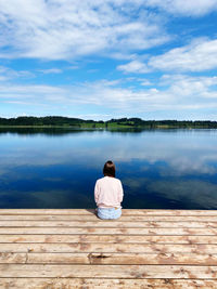 Rear view of man sitting on lake against sky
