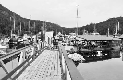 Sailboats moored on pier by lake against sky