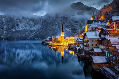 Panoramic view of illuminated buildings by lake against sky during winter