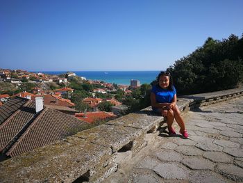 Portrait of mid adult woman sitting on retaining wall against city