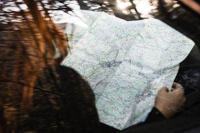 Unrecognizable female traveler sitting on passenger seat and reading tourist map while checking route during road trip through woodland