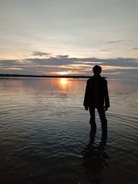 Silhouette man standing in sea against sky during sunset