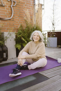 Happy senior woman sitting on exercise mat at terrace