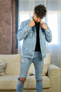 Young man wearing denim jacket while standing at home