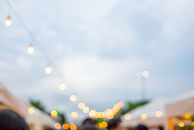 Defocused image of illuminated lights against sky in city