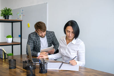 Office staff are sitting at a table with a laptop and making notes in a notebook