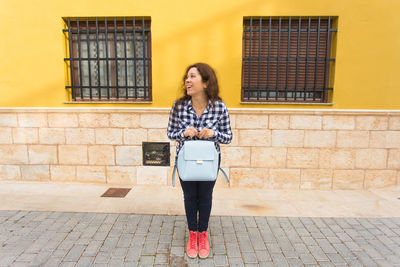 Full length portrait of woman standing against building