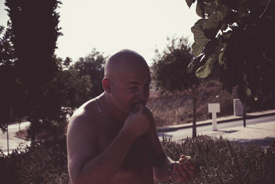 Shirtless mid adult man eating while standing outdoors
