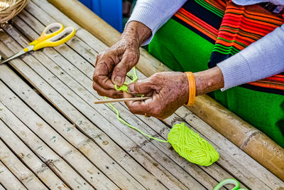 High angle view of senior woman tying knot of wool string over bamboo furniture