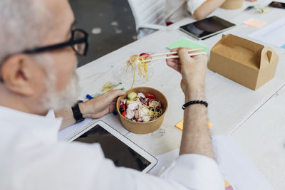 Businessman having poke bowl with chopsticks in lunch break at office