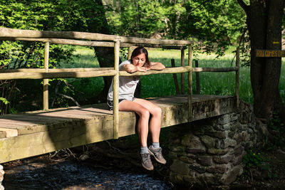 Portrait of woman sitting on wood against trees