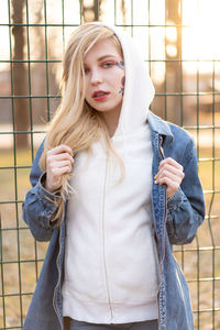 Portrait of beautiful young woman standing against fence