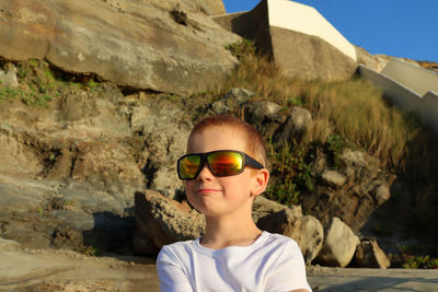A blond boy in sunglasses looks at the atlantic ocean and smiles.