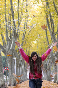 Portrait of young woman with arms raised standing in autumn