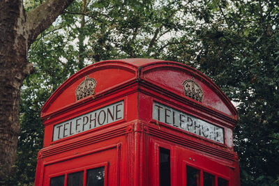 Low angle view of red telephone booth against trees