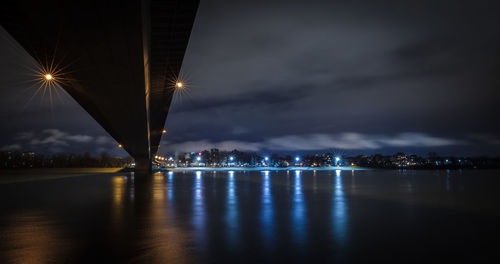 Illuminated city by river against sky at night