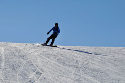 Full length of man snowboarding on snow covered field against clear sky