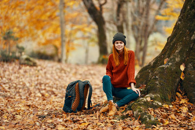 Young woman sitting on tree during autumn