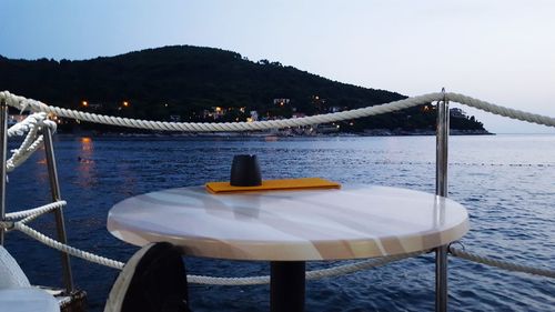 Chairs and table by sea against clear sky