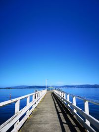 Pier over sea against clear blue sky