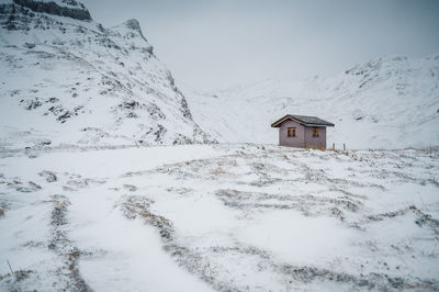 Snow covered house by mountain against sky