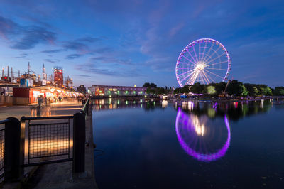 Illuminated ferris wheel by river against sky at night