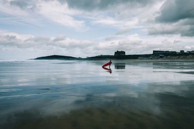 Mid distance view of person with surfboard at beach against sky