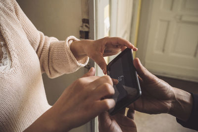 Midsection of customer signing on mobile phone during package delivery