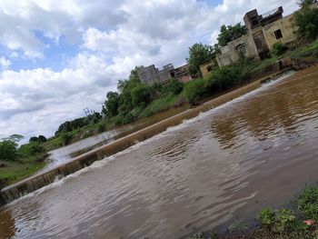 Scenic view of river amidst trees and buildings against sky