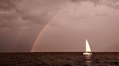 Sailboat sailing in sea against rainbow in sky