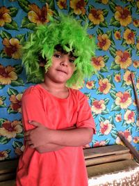 Portrait of boy wearing green wig while standing against patterned wall