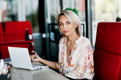 A beautiful girl works online on a laptop, sits in a cafe or office, uses a remote internet 