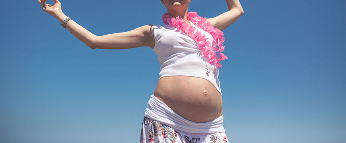 Midsection of pregnant woman with arms raised against clear sky