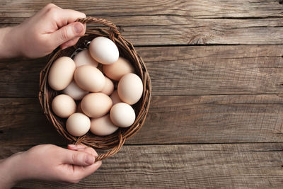 Flat lay with hands holding basket with organic chicken eggs on wooden background. organic household