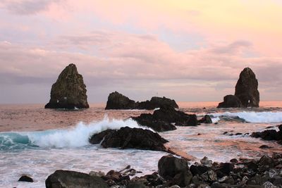 Rocks in sea against sky during sunset